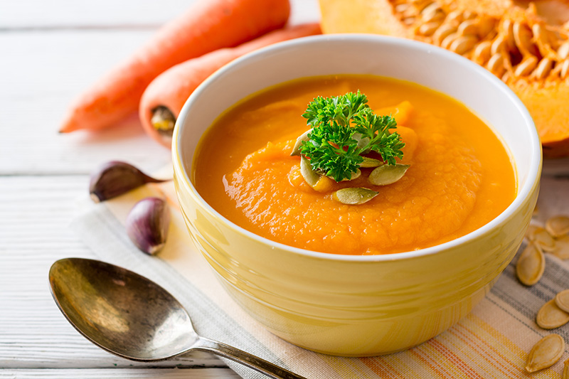 Pumpkin and carrot cream soup with pumpkin seeds and parsley in bowl on white wooden background. Selective focus.